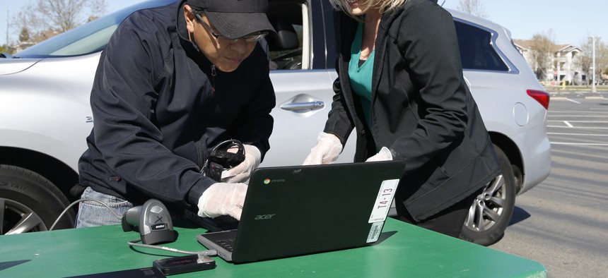 Wilbert Villalta, left, and Lindsey Lilley, right, employees of the Elk Grove Unified School District, register a Chromebook to be assigned to a student in the district, at Monterey Trail High School in Elk Grove, Calif., Thursday, April 2, 2020. 
