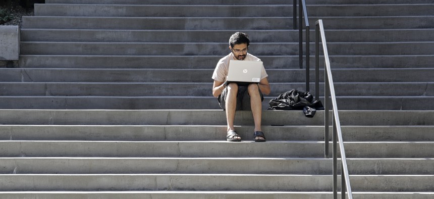 Amazon software engineer Aditya Iyer sits alone on steps outside the company headquarters as he works on his laptop Friday, March 20, 2020. 