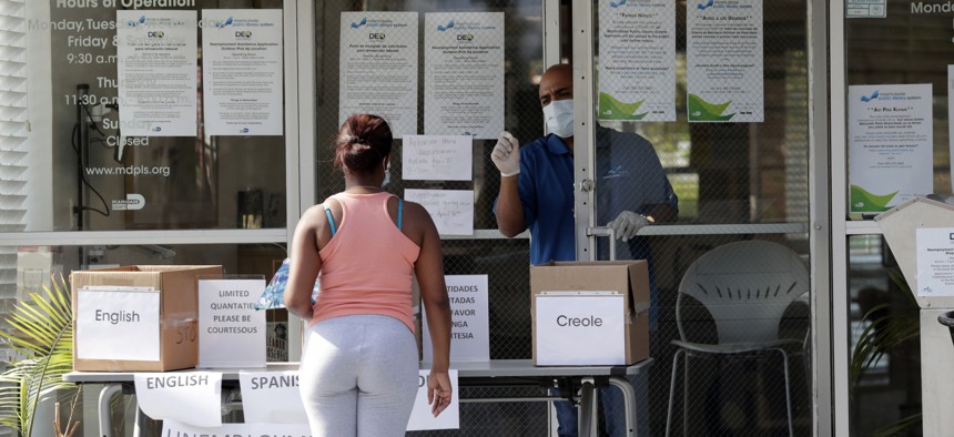 In this April 8, 2020 photo, Harry Varela, right, wears a protective mask as he talks with a woman requesting an unemployment form at a Miami-Dade County library during the new coronavirus pandemic in Miami. 