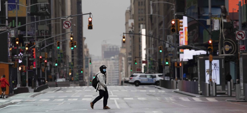 A man wearing a mask crosses the street in a quiet Times Square, Thursday, April 9, 2020, during the coronavirus epidemic. 