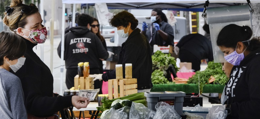 A mother and son wearing protective masks pay for fresh produce at a farmer's market in the North Hollywood section of Los Angeles on April 4, 2020. 