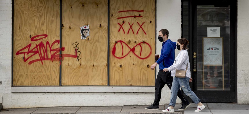 People in masks to protect against coronavirus, walk past a boarded up storefront along 14th Street in Northwest Washington, Wednesday, April 29, 2020.