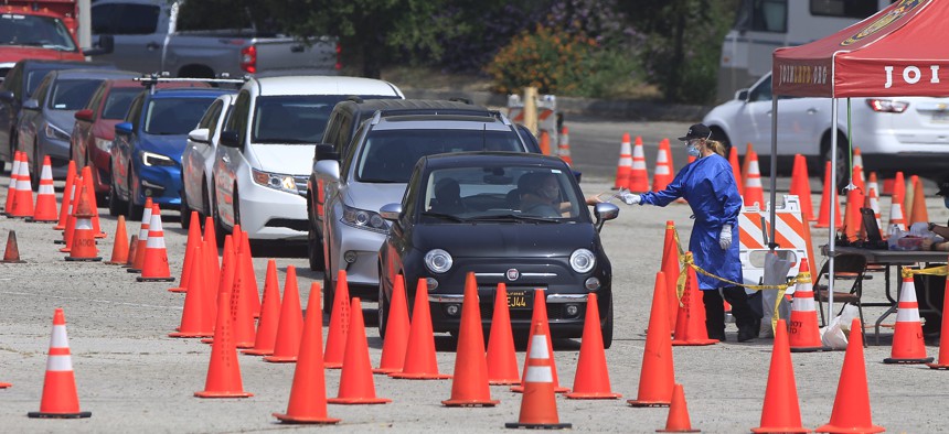 Los Angeles Fire Department officials wearing protective gear deliver testing kits to a waiting motorists at a COVID-19 drive-thru testing site in Elysian Park, Los Angeles on April 30, 2020. 