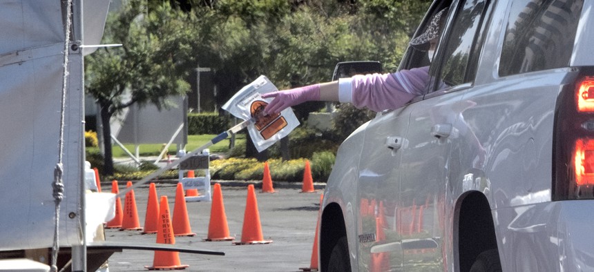In this Wednesday, May 6, 2020 photo a medical worker passes a self administered coronavirus test on a pole to a passenger in a car at a drive-thru testing site in the Woodland Hills section of Los Angeles. 