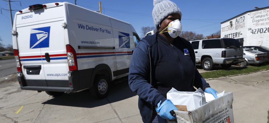 A United States Postal worker makes a delivery with gloves and a mask in Warren, Mich. on April 2, 2020.