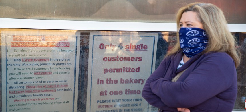 A masked customer waits in line next to a sign outlining the rules to enter at the Long's Bakery Shop in Indianapolis on May 1, 2020 after the bakery reopened after closing it doors due to COVID-19. 