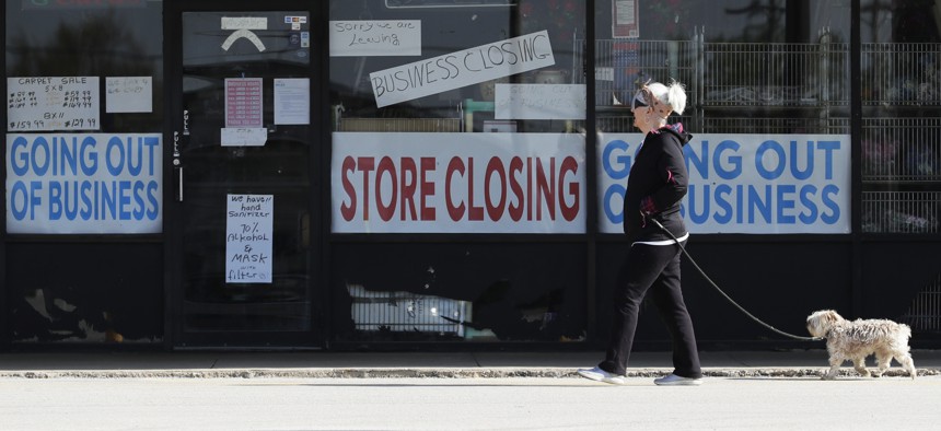 A woman takes walk with a dog in front of the closing signs displayed in a store's window front in Niles, Ill., Wednesday, May 13, 2020. 
