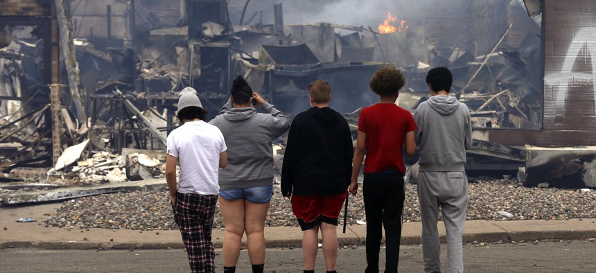 Onlookers watch as smoke smolders from a destroyed fast food restaurant near the Minneapolis Police Third Precinct on May 28, 2020, after a night of looting as protests continue over the death of George Floyd, who died in police custody on Monday.