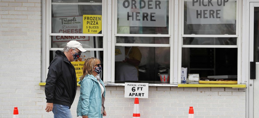 A couple, wearing protective masks due to COVID-19, walk through social distanced cones for patrons as they pass a seaside pizza shop, Monday, June 1, 2020, in Salisbury, Mass. 