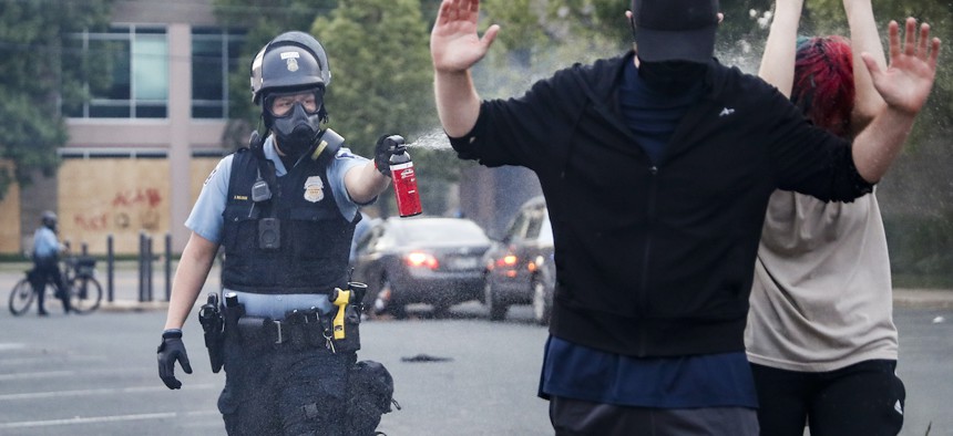 A police officer, Sunday, May 31, 2020, unloads pepper spray at protesters with their hands raised in Minneapolis