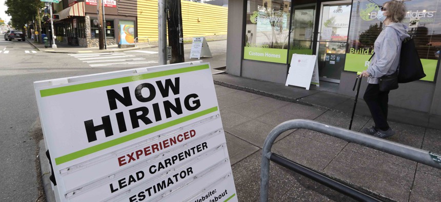 In this photo taken Thursday, June 4, 2020, a pedestrian wearing a mask walks past reader board advertising a job opening for a remodeling company, in Seattle. 