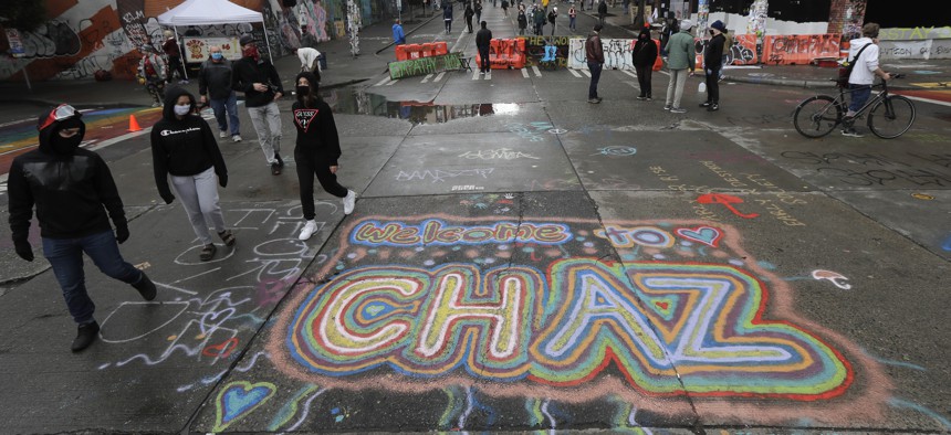 People walk past street art that reads "Welcome to CHAZ," Thursday, June 11, 2020, inside what is being called the "Capitol Hill Autonomous Zone" in Seattle. 