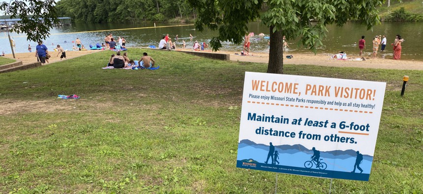 A sign instructs people to maintain a 6-foot distance from others while beachgoers lounge in Missouri’s Lake of the Ozarks State Park on May 30. The popular resort area made headlines for a viral video showing partiers disregarding Covid-19 guidelines.
