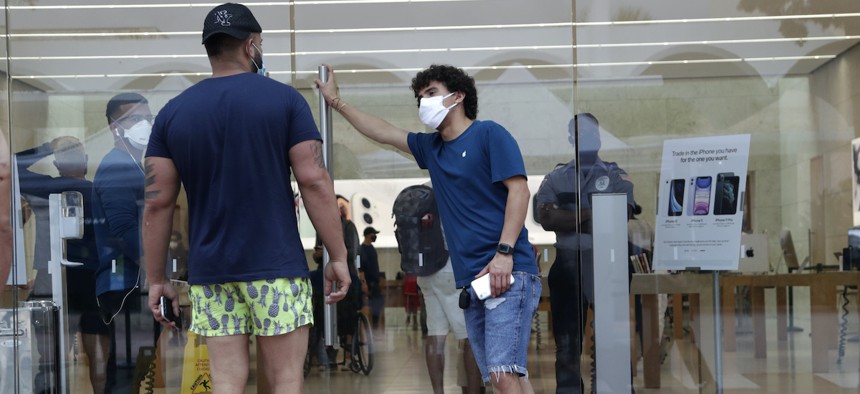 An employee wearing a protective face covering, right, monitors the flow of customers at an Apple retail store along Lincoln Road Mall during the new coronavirus pandemic, Wednesday, June 17, 2020, in Miami Beach, Fla. (AP Photo/Lynne Sladky)