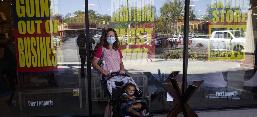 A shopper stands outside of a Pier 1 Imports store as going out of business signs are posted amid the coronavirus pandemic Wednesday, July 1, 2020, in Santa Clarita, Calif.
