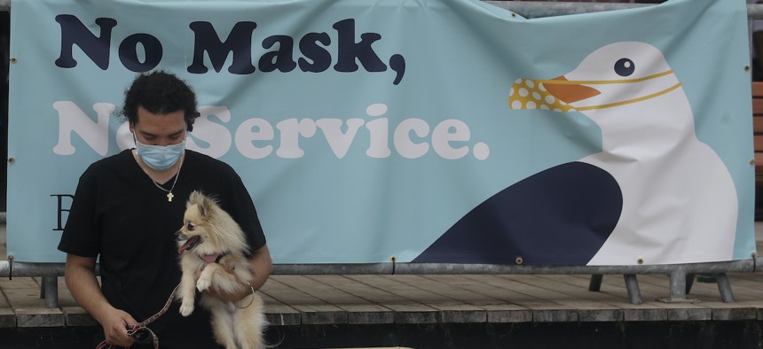Manny Munoz wears a mask while holding his dog Princess Diana in front of a sign at the Santa Cruz Beach Boardwalk during the coronavirus outbreak in Santa Cruz, Calif., Thursday, July 2, 2020.(AP Photo/Jeff Chiu)