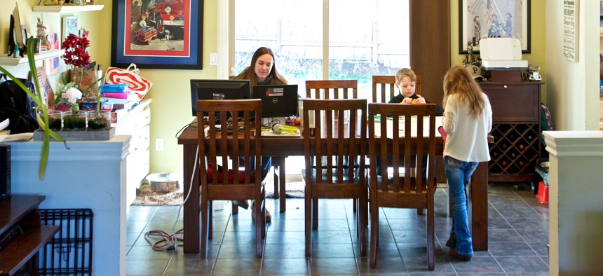 In this Tuesday, March 17, 2020 photo Kim Borton, left, works from home while her children Logan Borton, center, age 6 and Katie Borton, age 7, work on an art project in Beaverton, Ore.