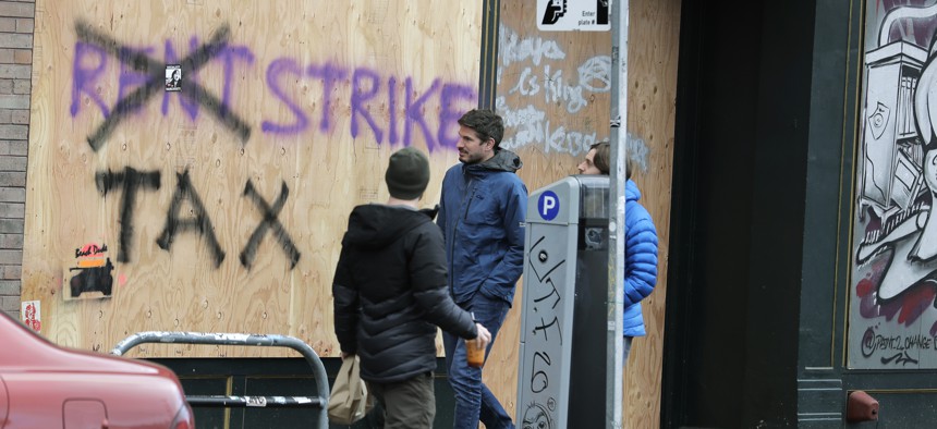 Pedestrians walk past graffiti advocating rent and tax strikes in Seattle.