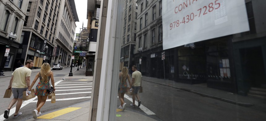 Passers-by walk near the glass storefront of an empty business location, in Boston's Downtown Crossing neighborhood, Sunday, Aug. 2, 2020.