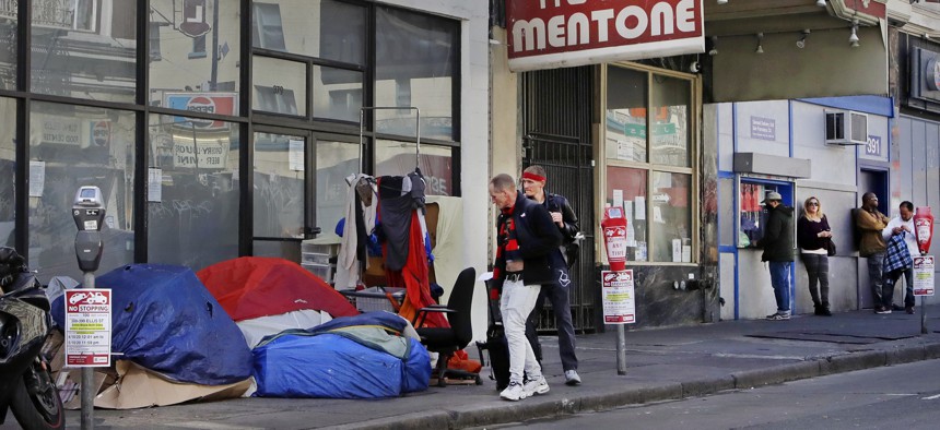 In this Monday, April 13, 2020, file photo, pedestrians walk to the edge of the sidewalk to avoid stepping on people in tents and sleeping bags in the Tenderloin area of San Francisco. 