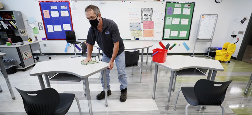 In this July 29, 2020 file photo, custodian Doug Blackmer wipes down a desk in a classroom at the Jesse Franklin Taylor Education Center in Des Moines, Iowa.