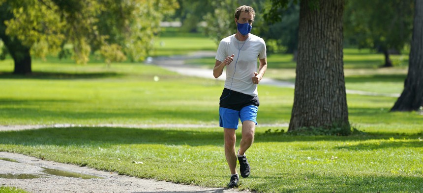 A lone runner wears a face covering while moving along a path in City Park early Friday, Aug. 28, 2020, in east Denver. (AP Photo/David Zalubowski)