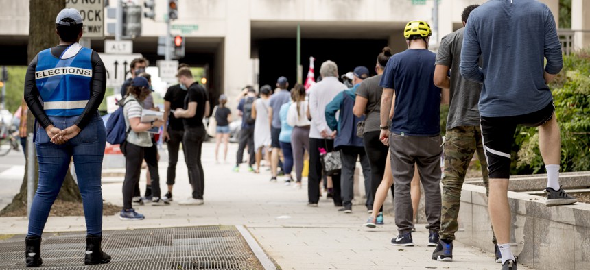 People wear masks as they wait in line to vote at a voting center during primary voting in Washington, Tuesday, June 2, 2020.