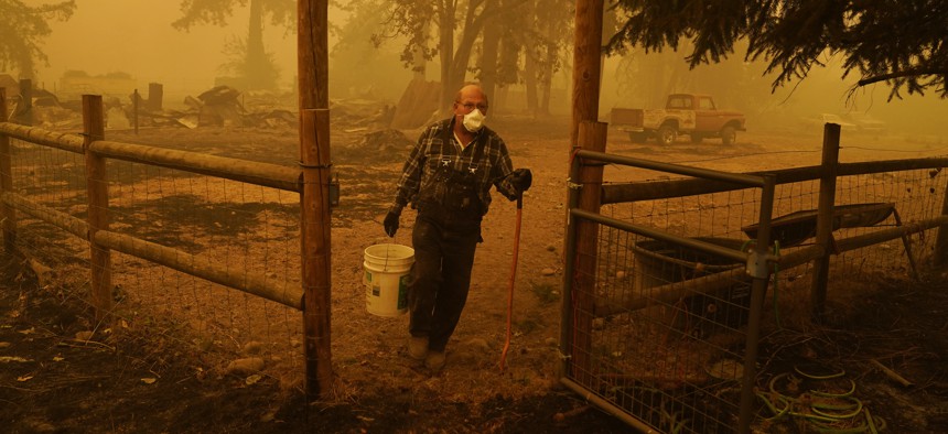 George Coble carries a bucket of water to put out a tree still smoldering on his property destroyed by a wildfire Saturday, Sept. 12, 2020, in Mill City, Ore.