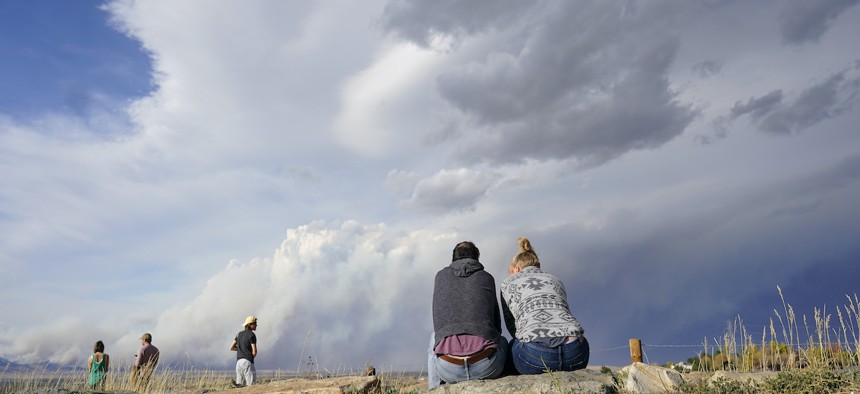 A couple sit on rocks at the overlook along Highway 36 to watch a smoke plume grow as several wildfires burn in northern and western Colorado and smoke funnels on to the eastern plains Saturday, Oct. 17, 2020, near Boulder, Colo. 