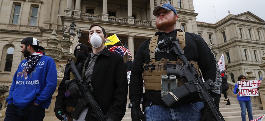 In this April 15, 2020 file photo, protesters carry guns outside the Capitol Building in Lansing, Mich. 