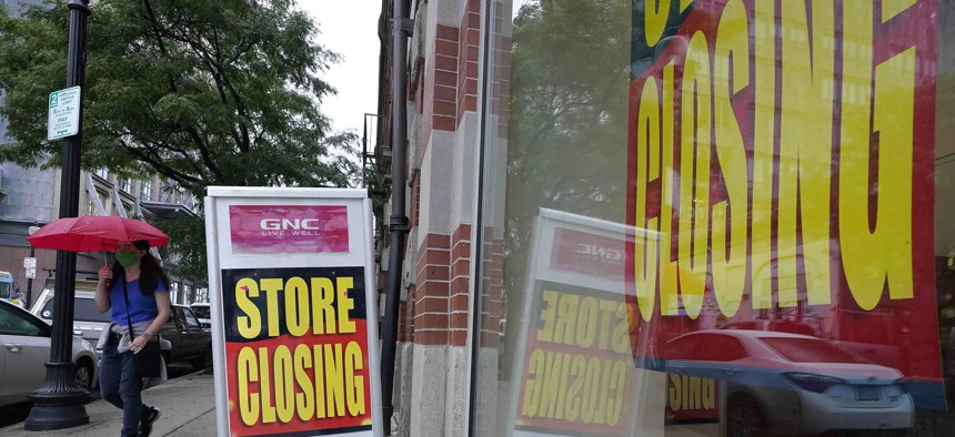 In this Sept. 2, 2020 photo a passerby walks past a business storefront with store closing signs in Boston. 