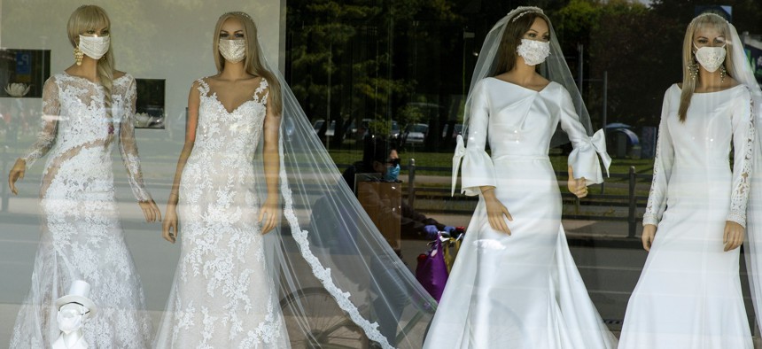A cyclist wearing a protective mask to protect against coronavirus is reflected in the window of a wedding dress store with mannequins wearing face masks on Thursday, April 23, 2020. 