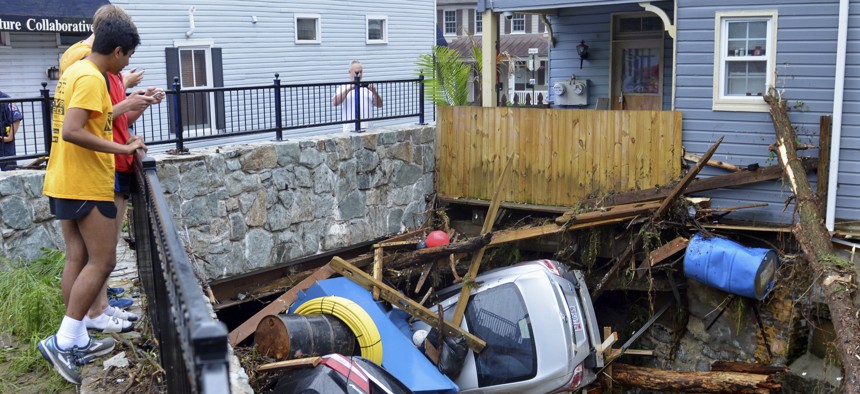 Residents on May 28, 2018 gather by a bridge to look at cars left crumpled in one of the tributaries of the Patapsco River that burst its banks as floodwaters channeled through historic Main Street in Ellicott City, Md. 