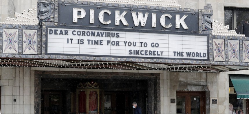 A man wears a mask as he walks in front of the Pickwick Theatre in Park Ridge, Ill., Tuesday, May 5, 2020. The cinema has been closed during the coronavirus pandemic.
