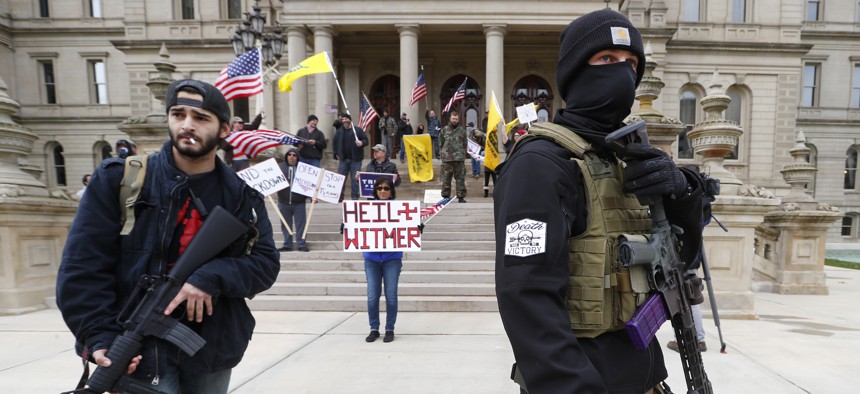 In this April 15, 2020, file photo protesters carry rifles near the steps of the Michigan State Capitol building in Lansing, Mich. 