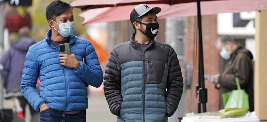 Pedestrians wearing masks walk past a small grocery store in the Chinatown-International District Thursday, Nov. 12, 2020, in Seattle.