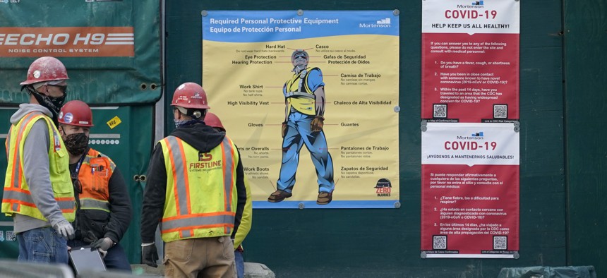 Construction workers wear masks as they stand next to posters with cautions about the spread of COVID-19, Thursday, Dec. 3, 2020.