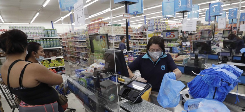 In this Wednesday, June 3, 2020 photo, a cashier bags groceries for customers at the Presidente Supermarket in the Little Havana neighborhood of Miami.