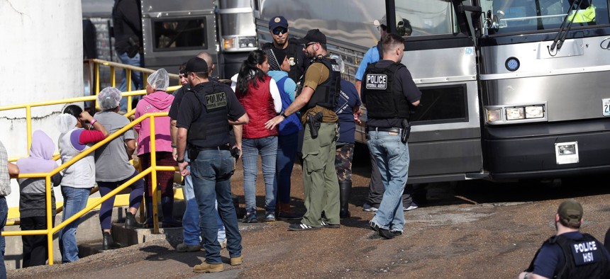 In this Wednesday, Aug. 7, 2019, file photo, handcuffed workers are escorted into a bus for transportation to a processing center following a raid by U.S. immigration officials at a Koch Foods Inc., plant in Morton, Miss. 