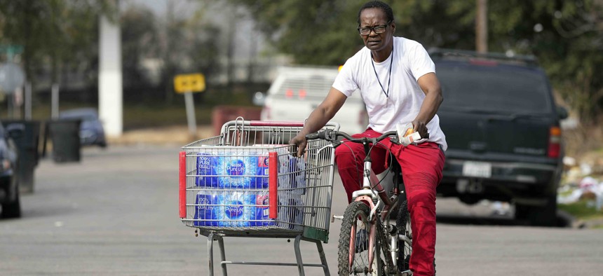 A Fifth Ward resident pulls a shopping cart with donated water back to her home Friday, Feb. 26, 2021, in Houston. 