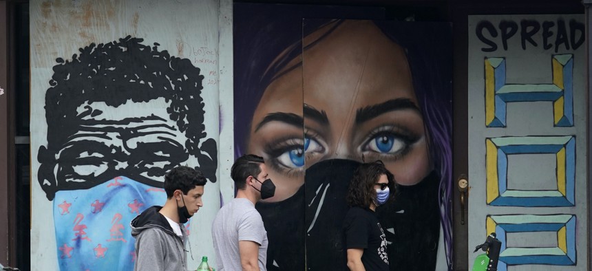 Pedestrians wearing masks to protect against the spread on COVID-19 pass murals painted on a boarded-up business in downtown Austin, Texas