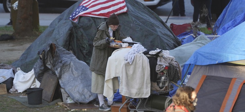 In this March 24, 2021, file photo a woman eats at her tent at the Echo Park homeless encampment at Echo Park Lake in Los Angeles. 