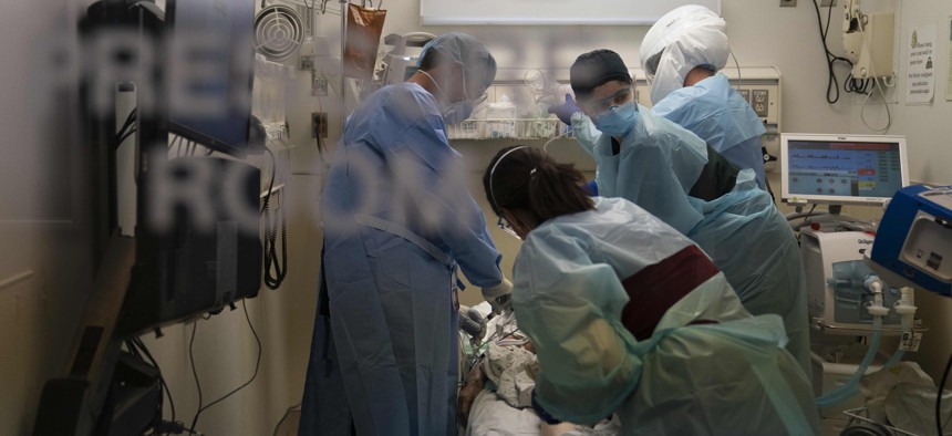 In this Nov. 19, 2020, photo, an EMT, second from right, looks at a monitor while performing chest compression on a patient who tested positive for coronavirus in a hospital emergency room.