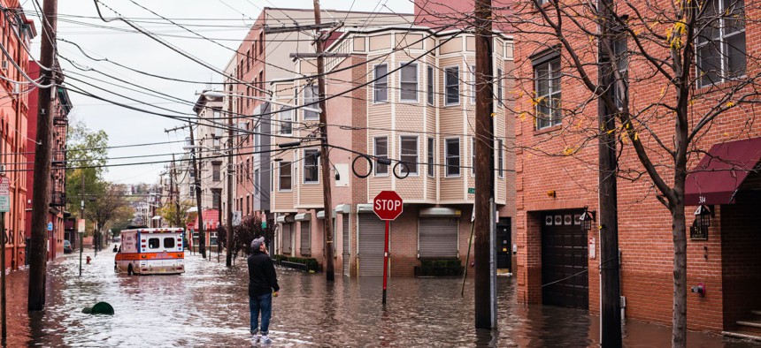 Hoboken, New Jersey, Man standing on the flooded street is talking to someone left in the building, ambulance car in the background.