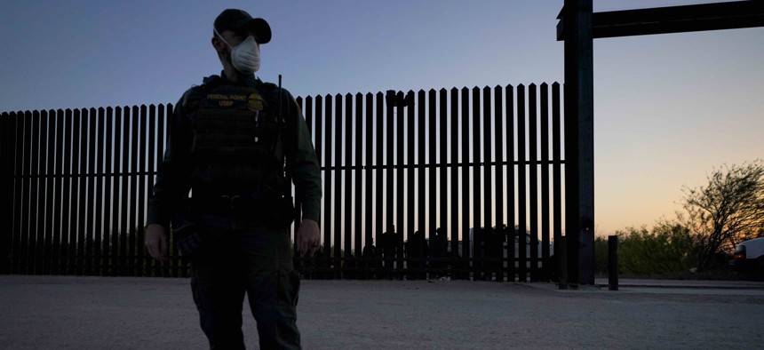 In this March 21, 2021 file photo, a U.S. Customs and Border Protection agent looks on near a gate on the U.S.-Mexico border wall as agents take migrants into custody, in Abram-Perezville, Texas. 