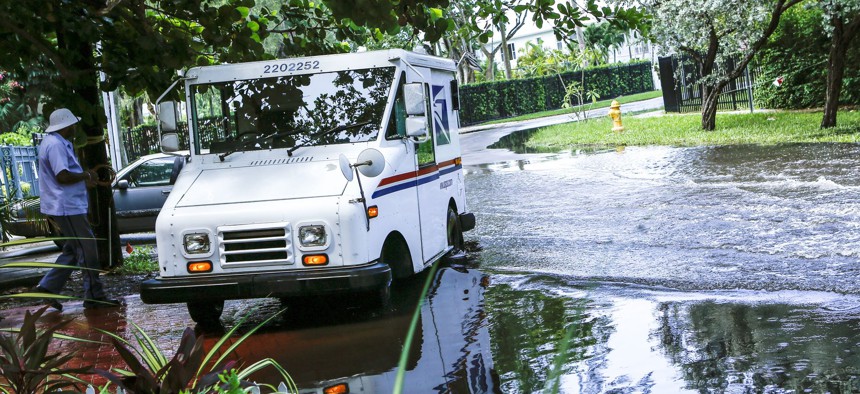 In this June 19, 2019 file photo, a postal worker returns to their truck parked on a flooded street in Miami caused by high tides.