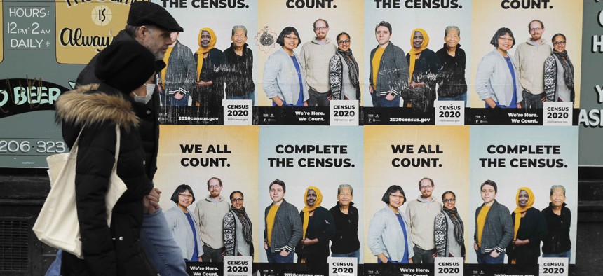 In this Wednesday, April 1, 2020 file photo, People walk past posters encouraging participation in the 2020 Census in Seattle's Capitol Hill neighborhood. 