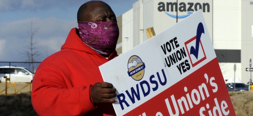 In this Feb. 9, 2021 photo ,Michael Foster of the Retail, Wholesale and Department Store Union holds a sign outside an Amazon facility where labor is trying to organize workers in Bessemer, Ala.