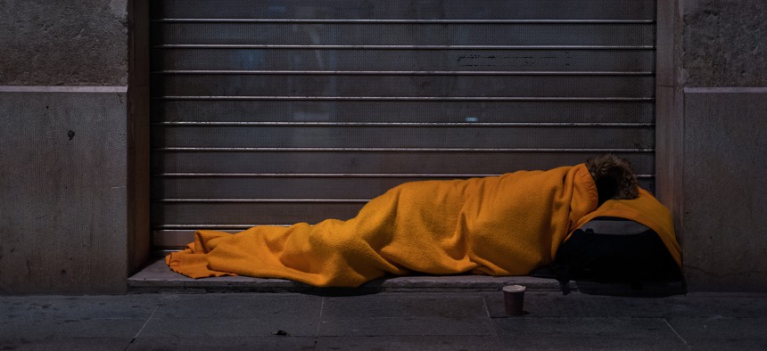 A homeless person sleeps on the street under a blanket.