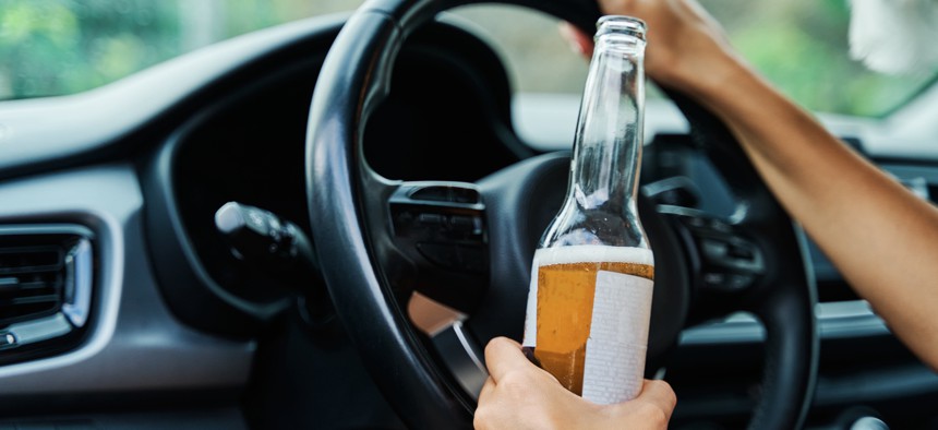 A young woman holding a beer while driving her car.
